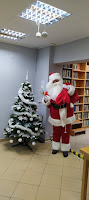 Święty Mikołaj pozujący do zdjęcia przy choince w Czytelni Biblioteki.
