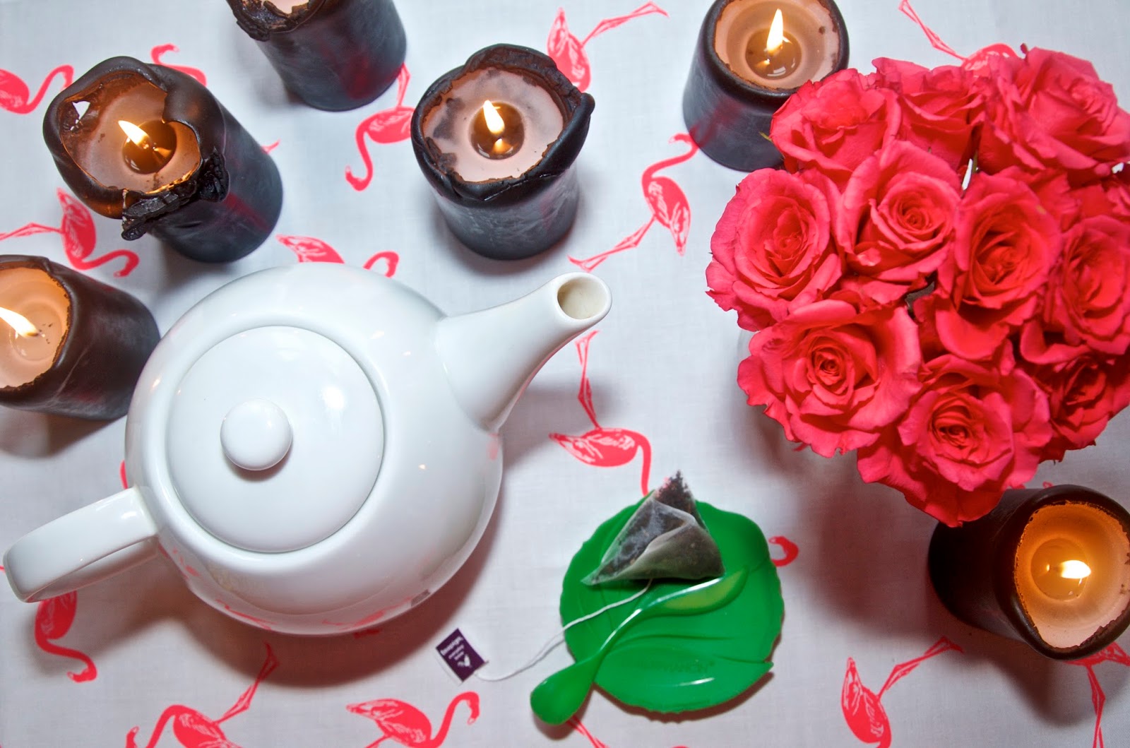 Pink roses, black candles, flamingo tea towel, teapot and tea bag on green saucer