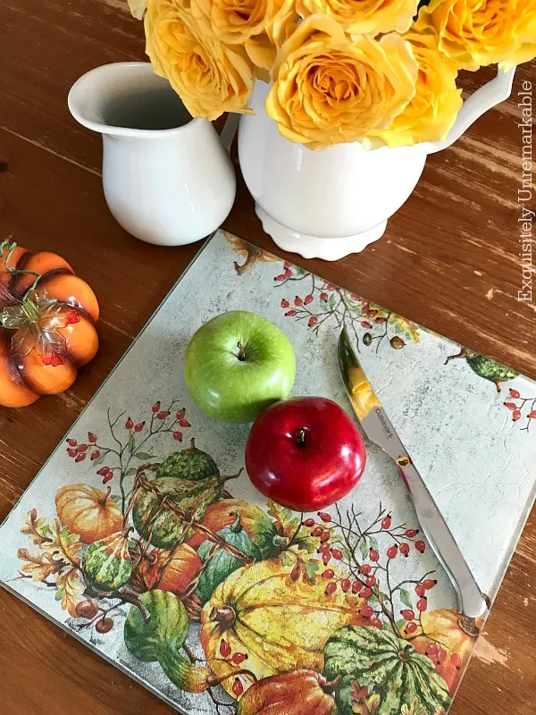 Napkin covered glass cutting board on table with fruit and flowers