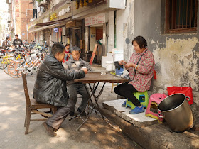 three people playing a card game on a sidewalk in Wuhan
