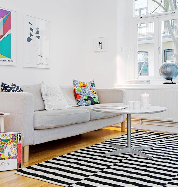 Living room in an apartment with a grey sofa, wood floors and a black and white striped rug and a round metal coffee table