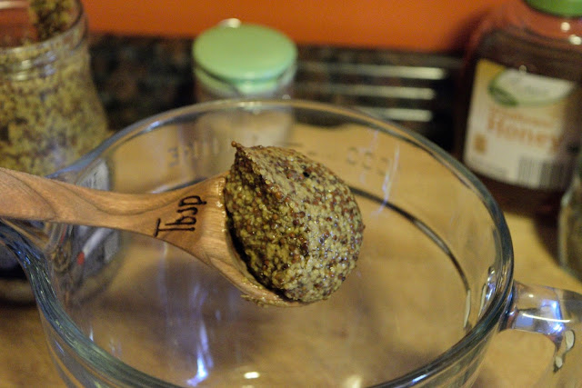 A tablespoon of whole grain Dijon mustard being added to a mixing bowl. 