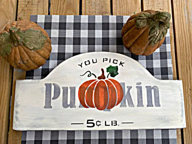 stenciled sign laying on table with pumpkins