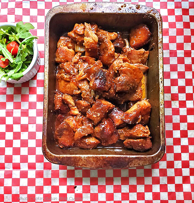 Glazed Pork Belly Burnt Ends This is an old roasting pan that has pork cubed made into burnt ends. It is glazed with a sweet shiny apricot, barbecue hot sauce and has a arugula salad with tomato on the side. This pan sits on a checkerboard napkin style paper
