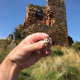 A picture showing a hand holding up a small ceramic skull with a view of Seafield Tower in the background.  Photo by Kevin Nosferatu for the Skulferatu Project.