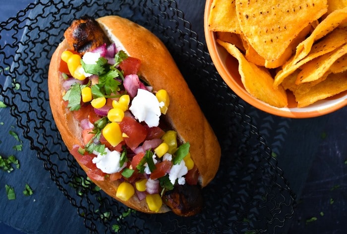 Vegan hot dog topped with salsa, corn and vegan feta