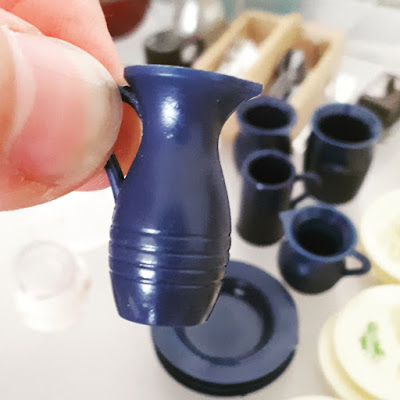 Finger and thumb holding a blue miniature jug. In the background are other pieces of the set.