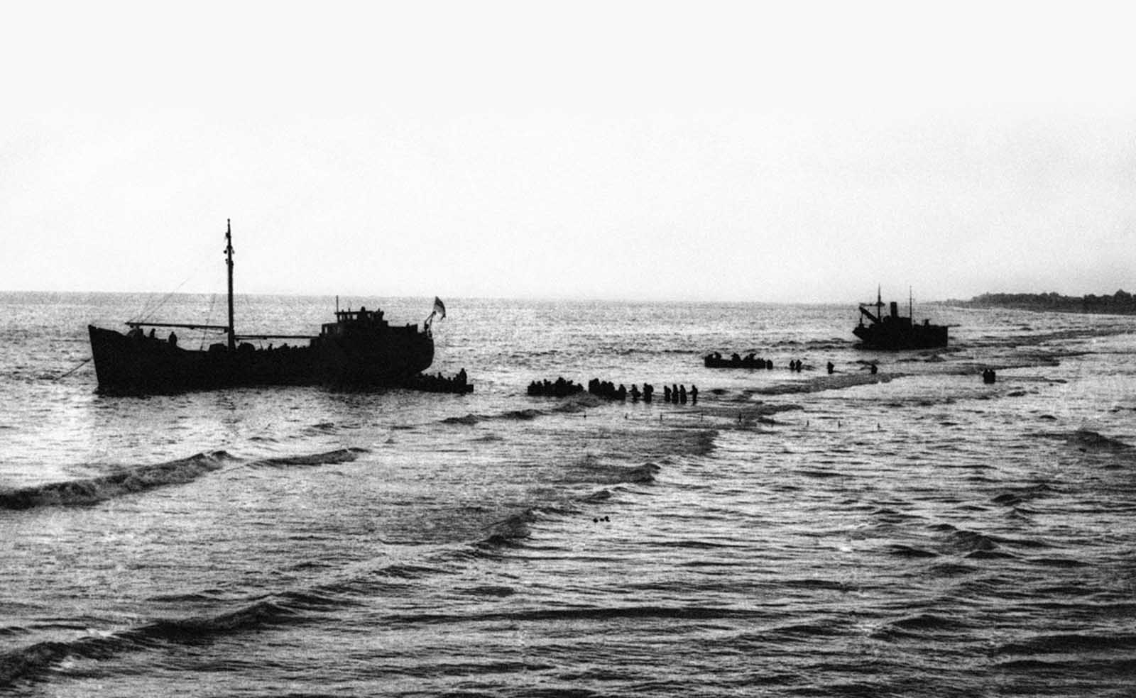 British and French troops wade through shallow water along the beach at Dunkirk, France on June 13, 1940 toward small rescue craft that will bring them to England. Some 700 private vessels joined dozens of military craft to ferry the men across the channel.