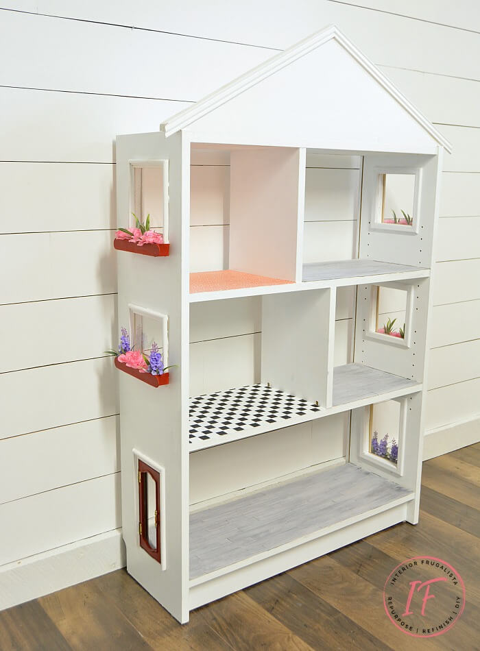 Turn an IKEA Billy Bookcase into a charming dollhouse with plexiglass windows, adorable window boxes, and a repurposed jewelry box chest front door.