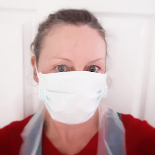 Writer in face mask and apron PPE, looking wry