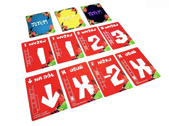 łatwa gra karciana dla dzieci na zdjęciu karty akcji w kolorze czerwonym rozłożone ukośnie po cztery w dwóch rzedach a nad nimi karty akcji w pozostałych kolorach, ułożone w trzy stosy