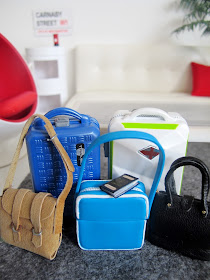 Modern dolls' house miniature living room with two suitcases, two handbags and a carry-on bag in the foreground.