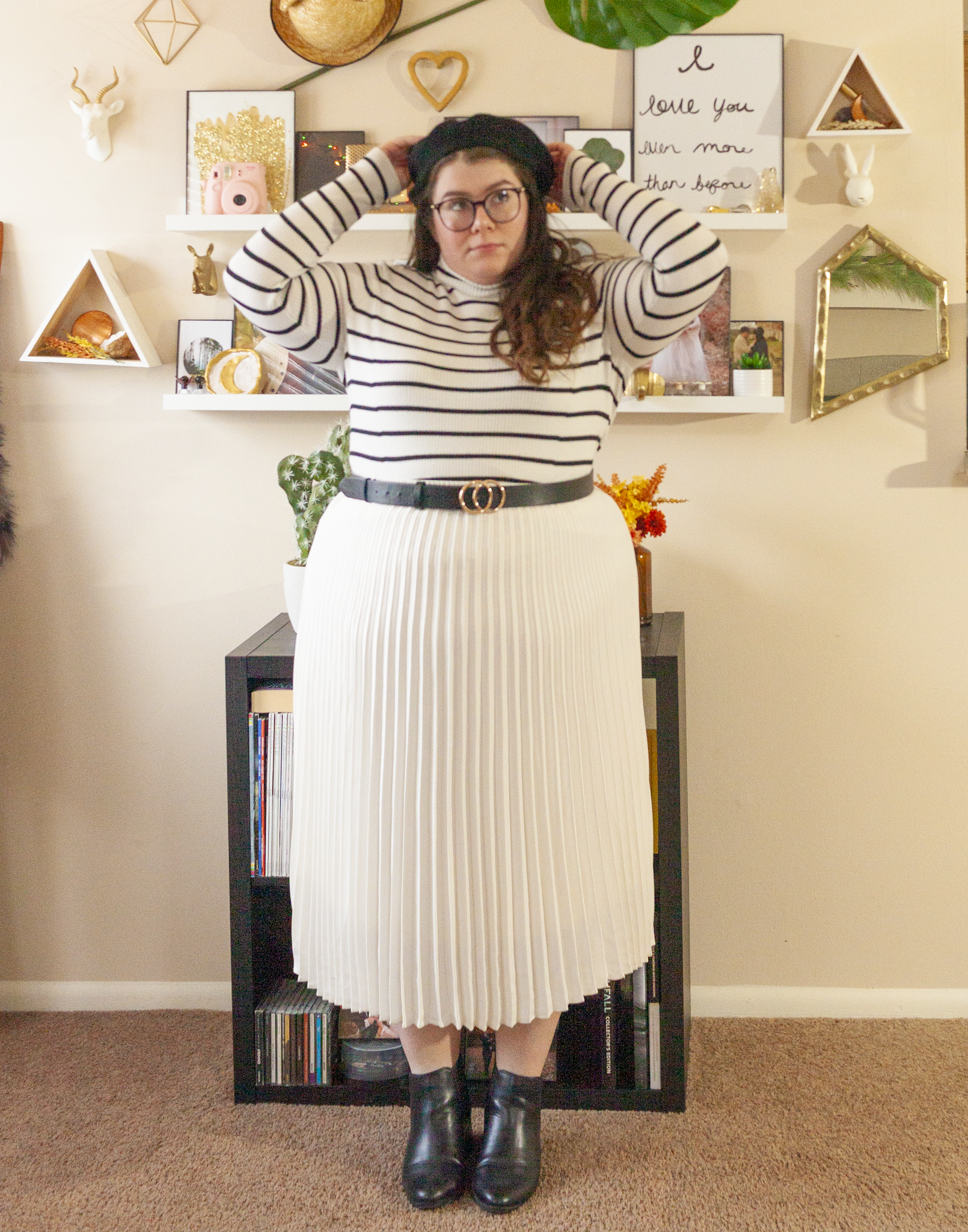 An outfit consisting of a black wool beret, a black on white striped lightweight turtleneck sweater tucked into a white pleated midi skirt and black chelsea boots.