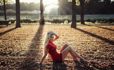 Chica rubia con vestido rojo sentada en parque mirando a cámara