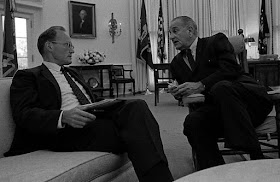 Two men in business suits seated in conversation in the Oval Offie