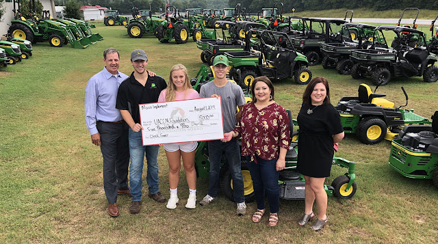 a group holding a large check standing in front of veichles