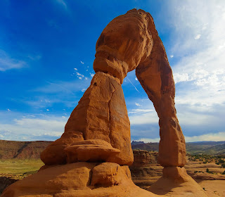 Large, natural rock arch against a blue sky with soft, brush stroke clouds