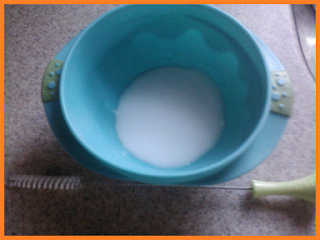 A blue bowl holding baking soda mixed with water at the top, and a straw cleaning brush with a green handle below.