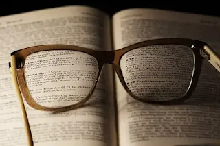 Imagem ilustrativa de um livro aberto sobre uma mesa com um óculos de grau aberto sobre este livro onde se pesquisa o artigo 4 da lei 12.112/09