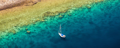 Visiter les plus belles plage : Vue aérienne, de la côte à Mayotte où un bateau à voile à jeté l'ancre, proche du lagon .