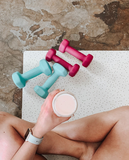woman sitting cross legged on fitness mat drinking protein shake 