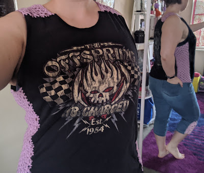 Woman wearing a bandshirt with crochet panel on shoulder and sides, standing in front of a mirror to capture the back too.
