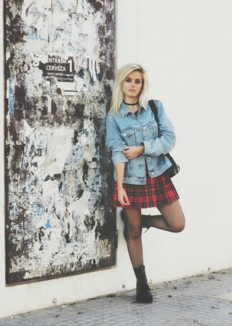 Estilo grunge con camiseta negra, falda de tablas tartán, medias de red grande, botas estilo militar y cazadora vaquera