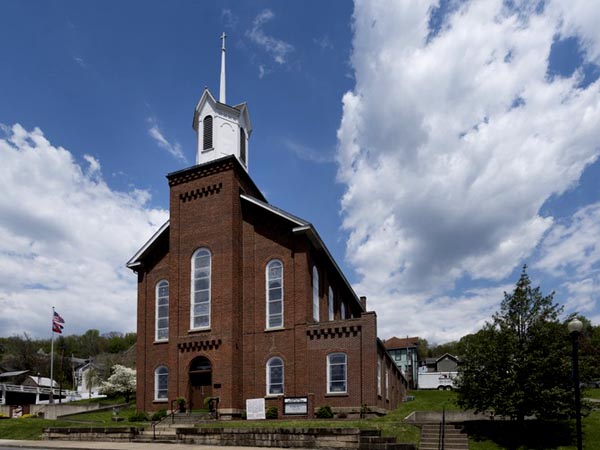 brick church with white steeple against blue sky with fluffy white clouds