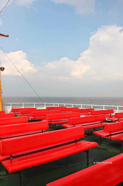Rows of red benches on the upper green painted deck of a passenger ferry.