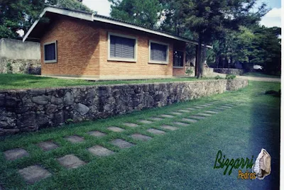 Muro de pedra com pedra moledo com a casa de tijolo a vista, o gramado com grama São Carlos e os caminhos do carro com pedra com junta de grama.