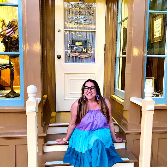 Jamie Allison Sanders sitting and smiling in front of the Sherman Brothers door at Main Street in Disneyland.