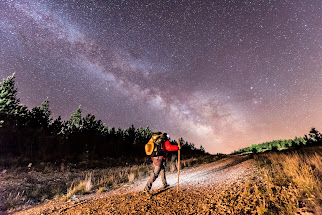 Peregrino con bastón recorriendo el Camino de Santiago de noche bajo un cielo estrellado.