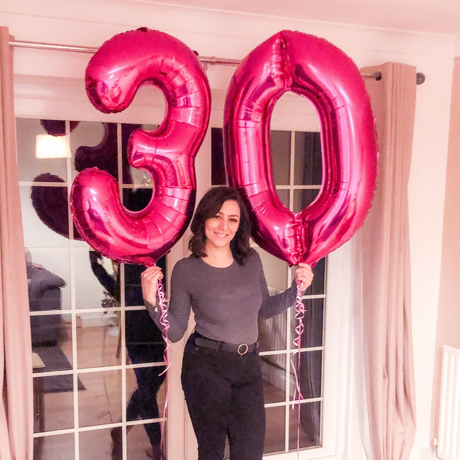 I'm holding two pink foil helium balloons writing out the number 30.
