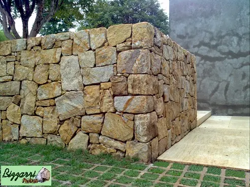 Detalhe do muro de pedra madeira amarela com o piso de pedra de mármore travertino.