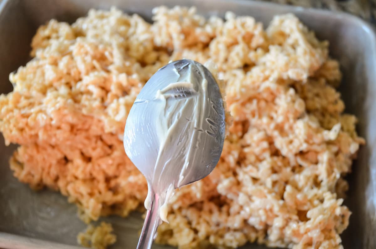 A buttered spoon held over a pan of Brown Butter Rice Krispy Treats.