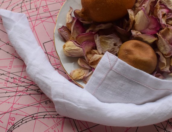 Aluslakanan kulmien ompelu. Kuvussa on vaalenpunaisen kaava-arkin päällä