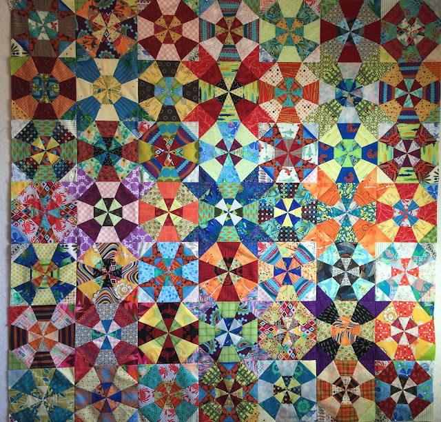 Kaleidoscope quilt creates illusions of overlapping circles. Brightly colored fabrics and tulip-like extensions make a lively kaleidoscope quilt