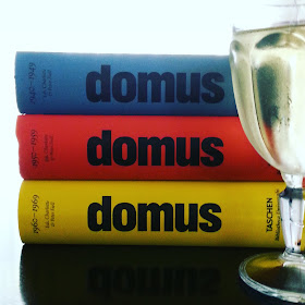 Stack of three domus books and a glass of wine on a coffee table.