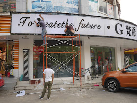 young men repairing a storefront sign with the words "To create the future"