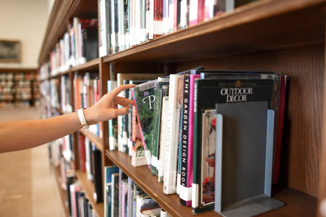 PERSON HOLDING BOOK FROM SHELF