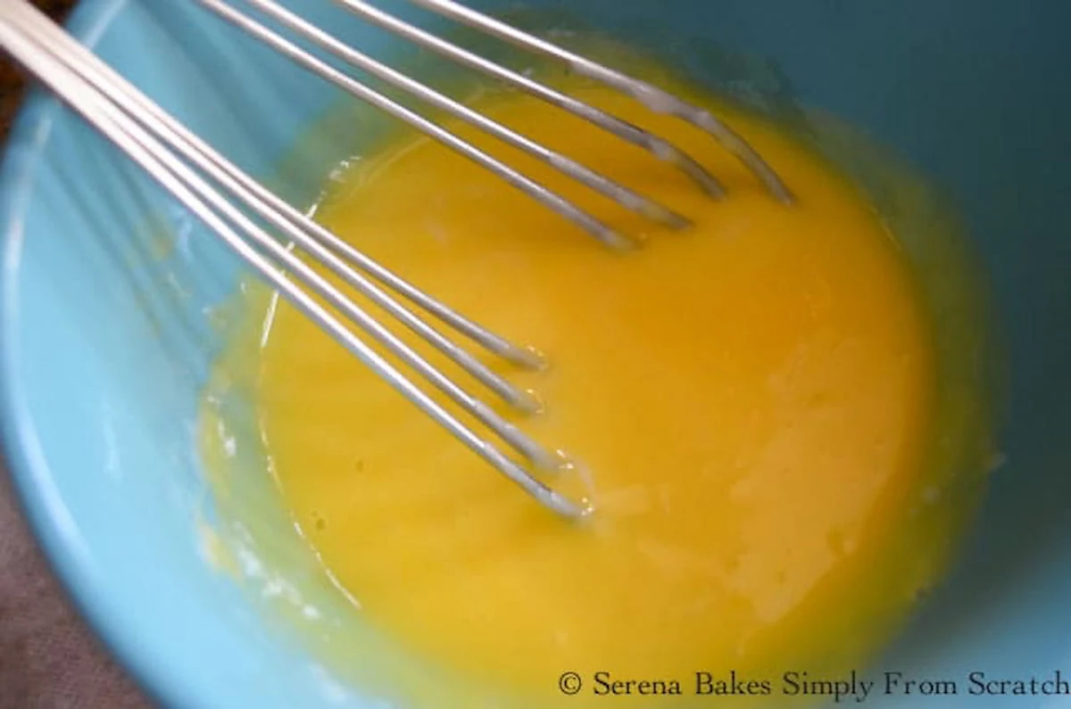 Cream mixture being stirred into eggs in a blue bowl.