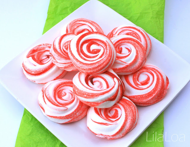 A white plate stacked with a batch of red and white striped peppermint meringue cookies on a green tablecloth