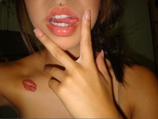 Foto de una mujer sacando la lengua lleva en su hombro un tatuaje de beso