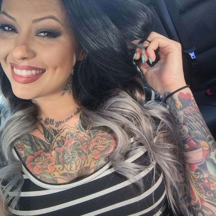 modelo latina, riendo, esta en su carro y lleva vestido playero, luce tatuajes en pecho y brazos