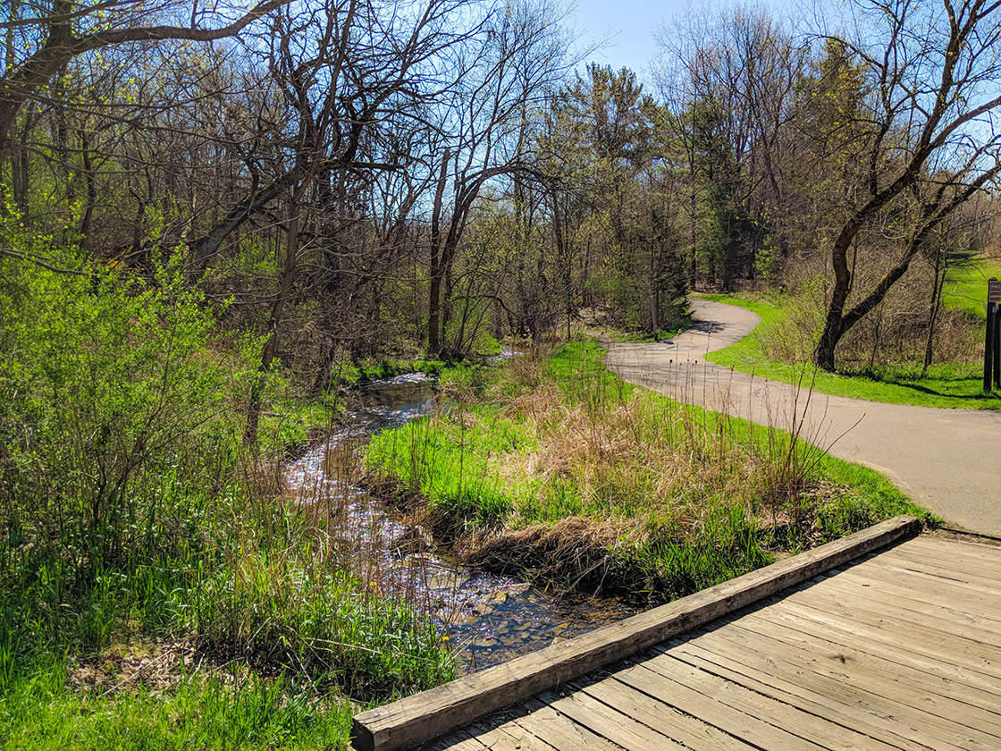 wood bridge over stream leading to paved trail
