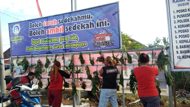 Mojokerto - Sikap gotong royong dan peduli sesama di masa pandemi Covid-19, kian mengakar kuat pada warga masyarakat Kabupaten Mojokerto. Aksi nyatanya langsung diaplikasikan dalam bentuk inovasi-inovasi unik dan bermanfaat. Salah satunya papan sayur gratis bagi warga, yang disiapkan di Kampung Tangguh Covid-19 Desa Gunungsari Kecamatan Dawarblandong. Selain sayur, disertakan juga papan nomer telepon tanggap darurat Covid-19.  Papan sayur gratis dengan motto “Ingat Saudaramu yang Lain, Ambil Seperlunya Taruh Semampunya” ini diinisiasi oleh Kawasan Rumah Pangan Lestari (KRPL) Kelompok Wanita Tani (KWT) Bunga Lestari Desa Gunungsari Kecamatan Dawarblandong.  KRPL sendiri diwujudkan dalam satu RT/RW dusun (kampung) yang telah menerapkan prinsip Rumah Pangan Lestasri dengan menambahkan intensifikasi pemanfatan pagar hidup, jalan desa, dan fasum lain. Misalnya sekolah, lahan terbuka hijau, serta mengembangkan pengolahan dan pemasaran hasil.  Meski sudah terbentuk sebelum adanya pandemi, Inovasi tersebut diharapkan mampu meringankan kebutuhan warga terdampak Covid-19 baik secara langsung maupun tidak langsung. Pemerintah Kabupaten Mojokerto pun, mengapresiasi dan terus mendorong desa-desa lain untuk terus berinovasi.  Wejangan ini disampaikan langsung oleh Bupati Mojokerto Pungkasiadi, saat menyerahkan bantuan APD dan logistik Covid-19 untuk Kampung Tangguh Gunungsari dan Kampung Tangguh Desa Pucuk Kecamatan Dawarblandong, Selasa (7/7) pagi.  “Kampung Tangguh untuk saat ini memang kita siagakan untuk penanggulangan Covid-19. Namun, sekalipun Covid-19 telah berhasil kita lalui nanti, saya ingin kampung ini tetap eksis dan mandiri. Potensi desa bisa hidup lagi. Kalau bisa, ciptakan lebih banyak inovasi,” kata bupati Pungkasiadi.  Bupati Pungkasiadi dalam arahanya juga menambahkan, pemotongan mata rantai Covid-19 harus dikerjakan bersama-sama dari seluruh elemen. Jelasnya, pemerintah daerah hanya bertindak sebagai pendorong dan pemberi stimulus. Namun, warga masyarakat lah yang paling tahu kondisi real di lapangan.    “Kami dari pemerintah, TNI dan Polri hanya mendukung panjenengan semua. Warga masyarakat lah yang paling tahu kondisi real lapangan. Namun kalau ada yang dibutuhkan, harus kita komunikasikan sama-sama. Kita ingin pandemi ini segera berakhir,” tambah bupati.  Sebagai informasi, sebelum menilik Kampung Tangguh Desa Gunungsari dan Desa Pucuk Kecamatan Dawarblandong, bupati sempat menerima penyerahan bantuan sembako penanggulangan Covid-19 dari PT. Ajinomoto berupa 15 ton beras dalam dua tahap. Pada masa pandemi ini, PT. Ajinomoto tetap beroperasi normal dengan menerapkan protokol kesehatan. Tidak ada PHK yang terjadi, namun kebijakan bekerja dari rumah atau work from home (WFH) demi keselamatan karyawan.  Untuk diketahui pula, kegiatan kunjungan Kampung Tangguh juga masih terus dilaksanakan. Sebelum hari Kamis, bupati juga telah melaksanakan peninjauan beberapa Kampung Tangguh di wilayah Kecamatan Pungging pada Senin 6 Juni lalu. Antara lain Desa Mojorejo, Desa Sekargadung dan Desa Jabontegal. (Jayak)