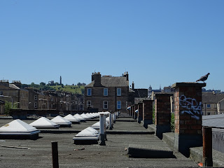 View from bridge over rooftops up to Calton Hill - view over the flat roof of a group of commercial units up to a hill with a monument standing on it.  Photo by Kevin Nosferatu for the Skulferatu Project