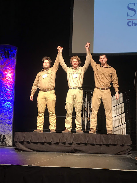 Three male students rise arms in celebration