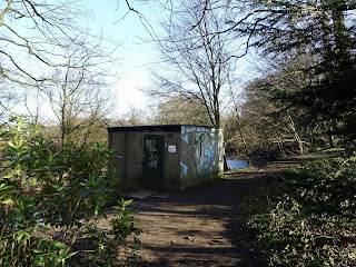 SEPA Monitoring Site, as seen from the riverbank by the River Almond.  It looks like a dull brick box with graffiti sprayed on the wall.  Photo by Kevin Nosferatu for the Skulferatu Project