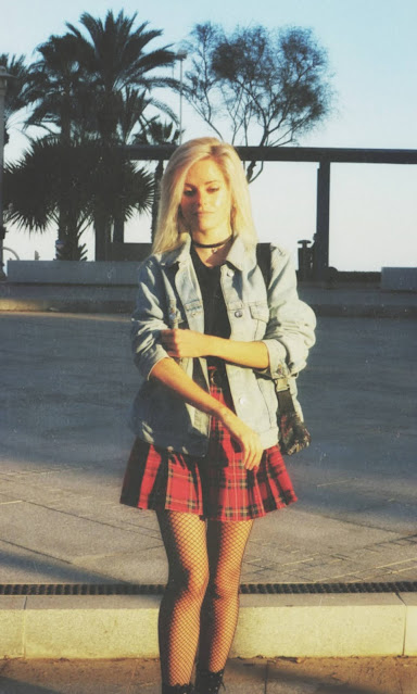 Estilo grunge con camiseta negra, falda de tablas tartán, medias de red grande, botas estilo militar y cazadora vaquera